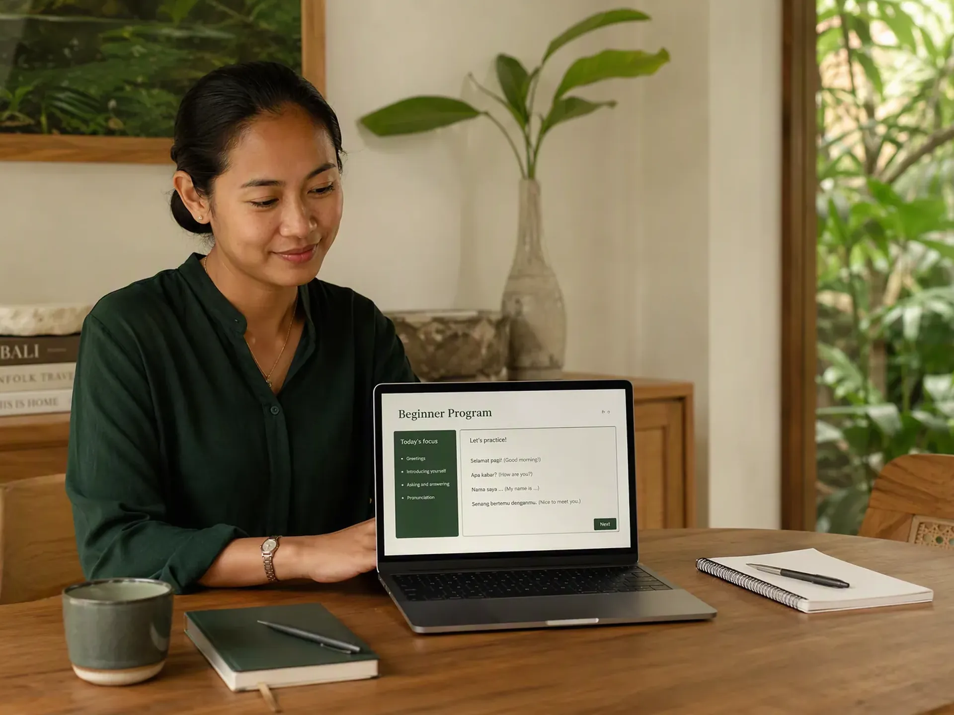 An Indonesian educator preparing a one-to-one lesson at an oak table in a bright Bali villa, with student books and learning materials on the table.