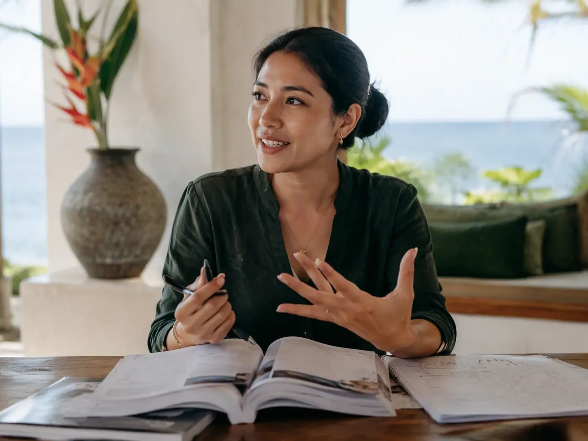 An Indonesian educator preparing a one-to-one lesson at an oak table in a bright Bali villa, with student books and learning materials on the table.