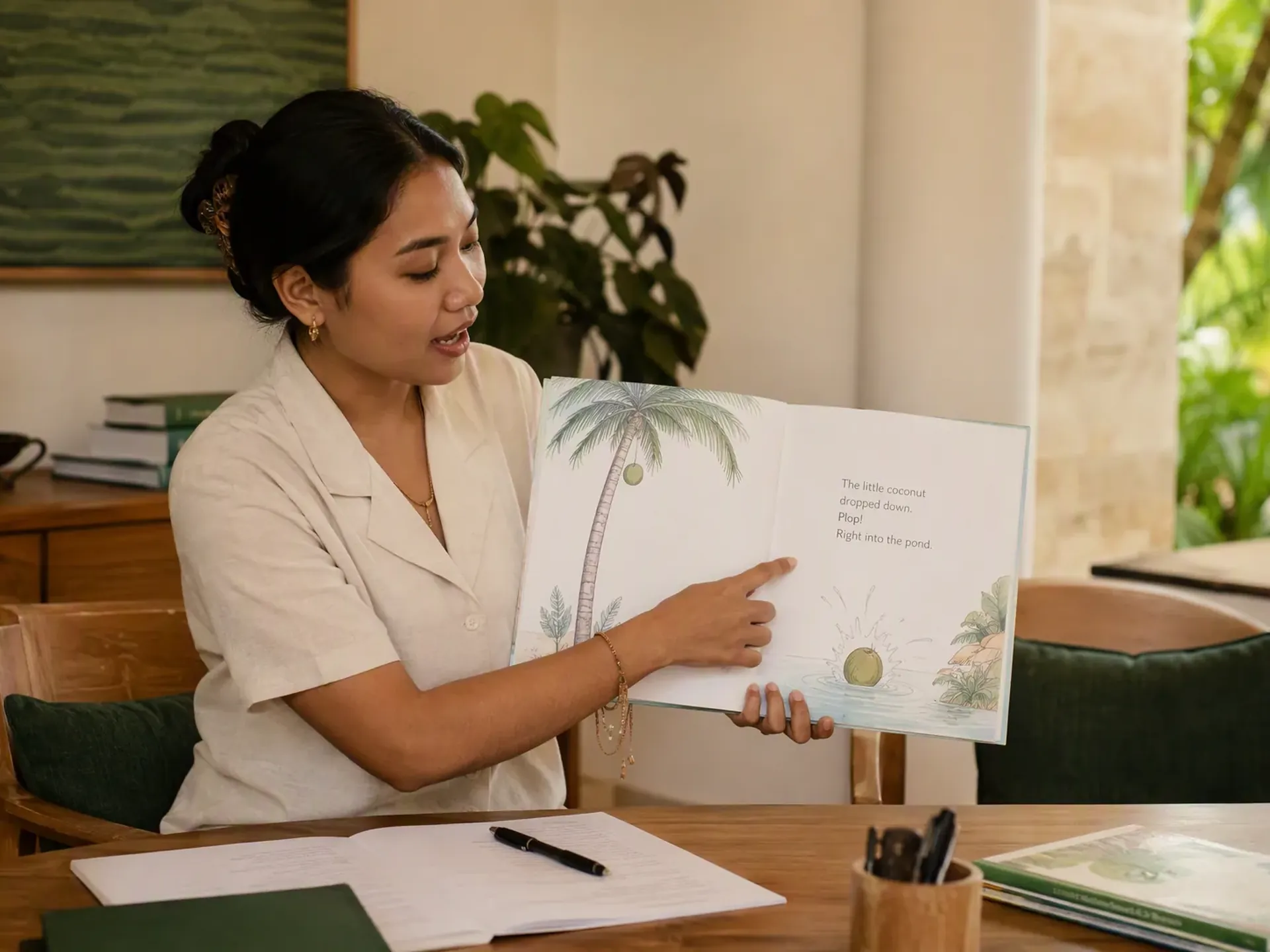 An Indonesian educator preparing a one-to-one lesson at an oak table in a bright Bali villa, with student books and learning materials on the table.